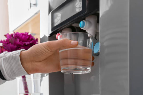 Woman filling glass from water cooler, closeup