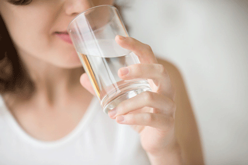 Smiling caucasian female model holding transparent glass in her hand.